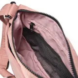 Bandolera grande color rosado confeccionada en textil nylon con acabado exterior con textura crinkle. Cuenta con cierre doble frontal, compartimento interior, herrajes de metal negro mate y correa ajustable y desmontable. Presenta un aplique rectangular negro con el logo de la marca grabado en el frente.
