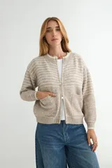 Campera tejida de punto con diseño a rayas horizontales en tonos beige y gris. Presenta cierre frontal completo, cuello redondo, bolsillos delanteros y puños y ruedo acanalados.