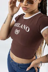 Remera ajustada de manga corta color marrón oscuro, con cuello redondo y ribetes blancos en el cuello y mangas. Presenta un estampado frontal en blanco con el texto "MILANO" y un escudo con el número "96".