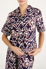 Camisa azul marino de manga corta, con cuello solapa, cierre frontal de botones y diseño estampado de estilo ikat en tonos blancos, rojos y azul marino.