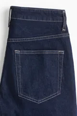 Jeans de cinco bolsillos en denim de algodón con leve stretch, color azul oscuro. Modelo de corte ajustado de cintura a muslo, más holgado de rodilla a bajo, con pierna acampanada (corte para bota) y tiro alto con cierre y botón.
