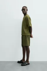 Camiseta de algodón de corte relajado (relaxed fit) con cuello redondo y manga corta. Presenta un tejido acanalado vertical (canalé) y un acabado ligeramente desgastado o lavado en tono verde oliva.