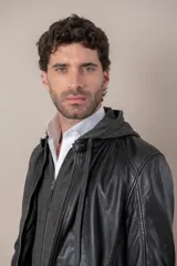 Campera de cuero negro con capucha gris desmontable, cierre frontal, bolsillos con cierre y detalles de hebillas en el cuello y la cintura.