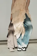 Vestido midi de escote en pico con lazada frontal y diseño sin mangas. Presenta múltiples niveles de volantes a lo largo de la falda y cierre lateral con cremallera oculta.