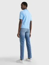 Chomba celeste de piqué de algodón con cuello ribeteado, cartera de cinco botones, logo de Tommy Hilfiger bordado en el pecho y bandera de Tommy Hilfiger bordada en la manga.