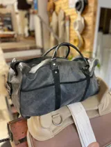 Bolso de viaje tipo duffel de cuero negro con detalles de refuerzo en gamuza y doble asa de mano.