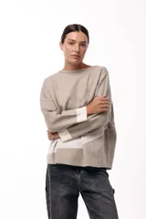 Sweater de punto con diseño de bloques de color en diagonal, combinando negro, beige y una franja central con textura metalizada. Presenta cuello redondo, mangas largas con puños en contraste y un corte holgado.