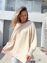 Sweater oversize de tejido de punto color crudo, con cuello redondo, manga larga con puños acanalados y detalle de costura vertical central. Presenta un diseño holgado con aberturas laterales en el ruedo.