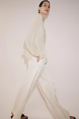 Blusa de viscosa color rosado con cuello redondo, manga larga abullonada con puños elásticos y cierre frontal con lazadas. Presenta un diseño con volantes en el bajo y corte asimétrico.