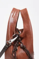 Bolso mediano de cuero marrón, tipo shopper, con detalles de cordones trenzados en la parte frontal y laterales, asa superior y logo plateado de la marca en la base.