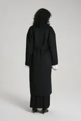 Tapado largo negro con cuello solapa, doble botonadura, cinturón y bolsillos laterales.
