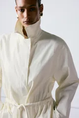 Trench oversize de cuello solapa y manga larga, con cintura ajustable mediante cordones y cierre frontal oculto. Cuenta con bolsillos laterales y forro interior.