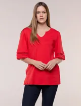Remera roja de algodón suave, de silueta recta, con escote en V y pequeña abertura. Cuenta con mangas de largo intermedio adornadas con una aplicación horizontal de puntilla calada y ruedo con tajos laterales.