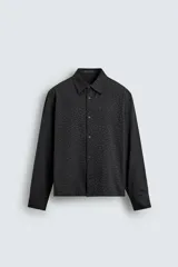 Camisa negra de corte relaxed fit, con cuello solapa y cierre frontal de botones, manga larga con puños abotonados y sutil patrón geométrico en jacquard.