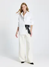 Camisa blanca de corte recto y estilo oversized, con cuello clásico, mangas largas con puños anchos, bolsillo delantero, cierre frontal con botones ocultos y bajo ligeramente redondeado.