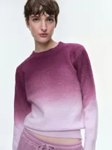 Buzo de tejido de punto con diseño degradé que transiciona de un tono morado oscuro a un rosa claro. Presenta cuello redondo, mangas largas y puños acanalados, con un corte holgado y cómodo.