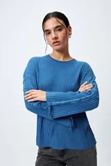 Sweater color crema de tejido de canalé con detalle de trenzado en las mangas y terminación con lazo ajustable.