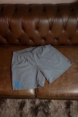 Short deportivo gris melange con cintura elástica y aberturas laterales para mayor movilidad. Presenta un logo de alas estampado en color azul en la parte inferior izquierda.