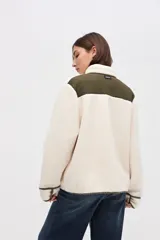 Campera de sherpa doble faz en color crema con detalles en verde oliva. Presenta cierre frontal con botones, bolsillos laterales de nylon capitoneado y terminaciones en contratono. Diseño de calce relajado con bordado en la manga.