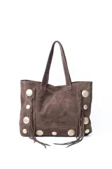 Cartera estilo shopper confeccionada en gamuza color marrón, con diseño boho que incluye flecos laterales y apliques metálicos circulares. Cuenta con doble asa de hombro.
