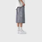 Bermuda baggy de denim color gris, de corte holgado y estilo urbano, con bolsillos laterales tipo cargo y detalle de bordado de la marca en el bolsillo trasero.