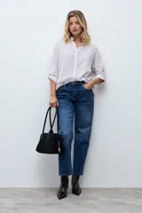 Camisa de corte holgado con diseño de rayas verticales en tonos beige y blanco, con sutiles destellos brillantes. Presenta cuello clásico, cierre frontal con botones y mangas largas con puños ajustables.