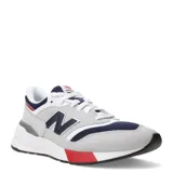Championes urbanos New Balance modelo 997R, con diseño inspirado en el running de los años 90. Presentan una combinación de colores gris, azul marino, blanco y detalles en rojo. Confeccionados con paneles de gamuza y malla textil, cuentan con el logo N en los laterales y suela de goma con amortiguación.