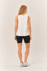 Conjunto deportivo de mujer compuesto por una musculosa blanca de cuello redondo con aberturas laterales y unos shorts biker negros ajustados de tiro alto con bolsillos laterales.