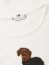 Remera de manga corta Tommy Hilfiger en color blanco, confeccionada en algodón regenerativo. Presenta un diseño clásico con cuello redondo y un estampado central distintivo de un perro salchicha con ropa.