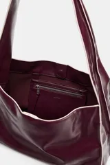 Bolso tipo shopper en formato horizontal, de efecto acharolado en color bordó con detalles de pespuntes en contraste. Cuenta con asa ancha de hombro, bolsillo interior con cierre y cierre principal con botón imantado.