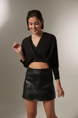 Blusa cropped de color negro, con cuello en V, mangas largas con puños ajustados y detalle de frunces en el frente.