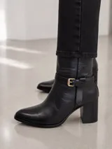 Bota de caña media confeccionada en cuero, con punta almendrada y taco cuadrado de 7 cm. Presenta una tira decorativa con hebilla metálica dorada en la zona del tobillo.
