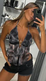 Top halter de tela liviana con estampado tie-dye en tonos grises, negros y rosados. Presenta un escote pronunciado con un aro metálico central y frunces que generan caída en la parte inferior.