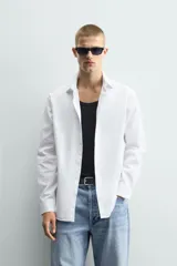 Camisa de corte slim fit confeccionada en tejido de algodón con textura. Presenta cuello italiano, manga larga con puños abotonados y cierre frontal de botones.