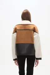 Chaqueta estilo aviador o biker, con paneles de color marrón (simil gamuza), negro (simil cuero acolchado) y blanco (simil borrego/sherpa). Presenta cuello solapa ancho forrado en blanco, detalles de hebillas negras en los hombros y cierres metálicos en la parte delantera.