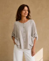 Blusa beige de lino de corte holgado y silueta oversize, con cuello redondo, cierre frontal de botones, bolsillos aplicados grandes y mangas tres cuartos con detalles de perforaciones bordadas en las mangas y el ruedo.