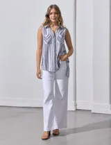 Camisa sin mangas de corte holgado, confeccionada en una mezcla de rayón y lino. Presenta un diseño a rayas verticales, cuello con solapa, escote en V y cierre frontal con botones. Incluye dos bolsillos frontales aplicados y aberturas laterales en el ruedo con detalle de botones.