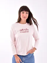 Remera de manga larga color blanco, con cuello redondo y estampa frontal en tono rosado que incluye un diseño de marco con moño y la frase "live simply love sincerely".