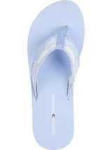 Ojotas de mujer con base celeste claro y suela con detalles de franjas blancas. Tira de tela con diseño geométrico en blanco y celeste, y logo de Tommy Hilfiger impreso en la plantilla.