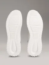 Zapatillas Calvin Klein modelo Eva Runner de color gris, confeccionadas en malla técnica transpirable con detalles en negro y salmón. Presentan suela blanca de EVA ultraligera, cordones negros y el logo 'cK' en el talón.