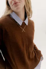 Buzo de lambswool color marrón, con escote redondo y detalle en V con cambio de punto y cadenetas en contratono. Tiene puños con cierres metálicos y tajitos laterales.