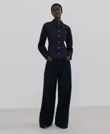 Camisa de denim azul oscuro, con cuello camisero, cierre frontal con botones y mangas largas ajustadas.