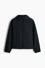 Campera rompevientos de nylon color negro, repelente al agua, con capucha ajustable con cordón, cierre frontal y bolsillos laterales. Cuenta con elásticos en los puños y forro interno.