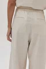 Pantalón de lino color beige, de pierna ancha, con botón en la cintura, pinzas en el frente y bolsillos delanteros y traseros.