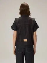 Chaleco negro con diseño de alamares frontales, costuras a la vista en contraste y volados en los hombros.