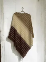 Poncho de hilo con diseño de franjas diagonales en tonos degradados de marrón, crema y beige, con textura tejida y terminación de flecos en el borde.