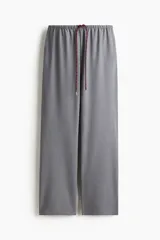 Pantalón de corte holgado color gris, con cintura elástica y cordón de ajuste trenzado en tonos rojo y blanco. Presenta piernas rectas y bolsillos laterales.