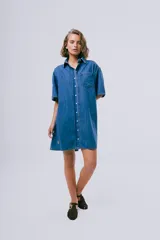 Vestido corto de denim azul oscuro, con cuello camisero, mangas cortas, cierre frontal con botones, bolsillo aplicado en el pecho y calce holgado.