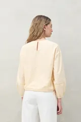 Blusa color verde claro de algodón con cuello a la base y bordados calados en el canesú. Presenta mangas largas con pequeñas aberturas lineales y ajuste con elástico en el puño.