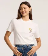 Remera blanca de manga corta y cuello redondo con un gran estampado trasero inspirado en el Tamagotchi, con texto en japonés y elementos gráficos de estilo retro.